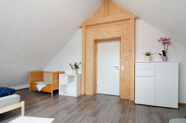 A room with a sloped ceiling, a wooden door, a white wardrobe, a wooden bed, a white cabinet, and two potted plants.