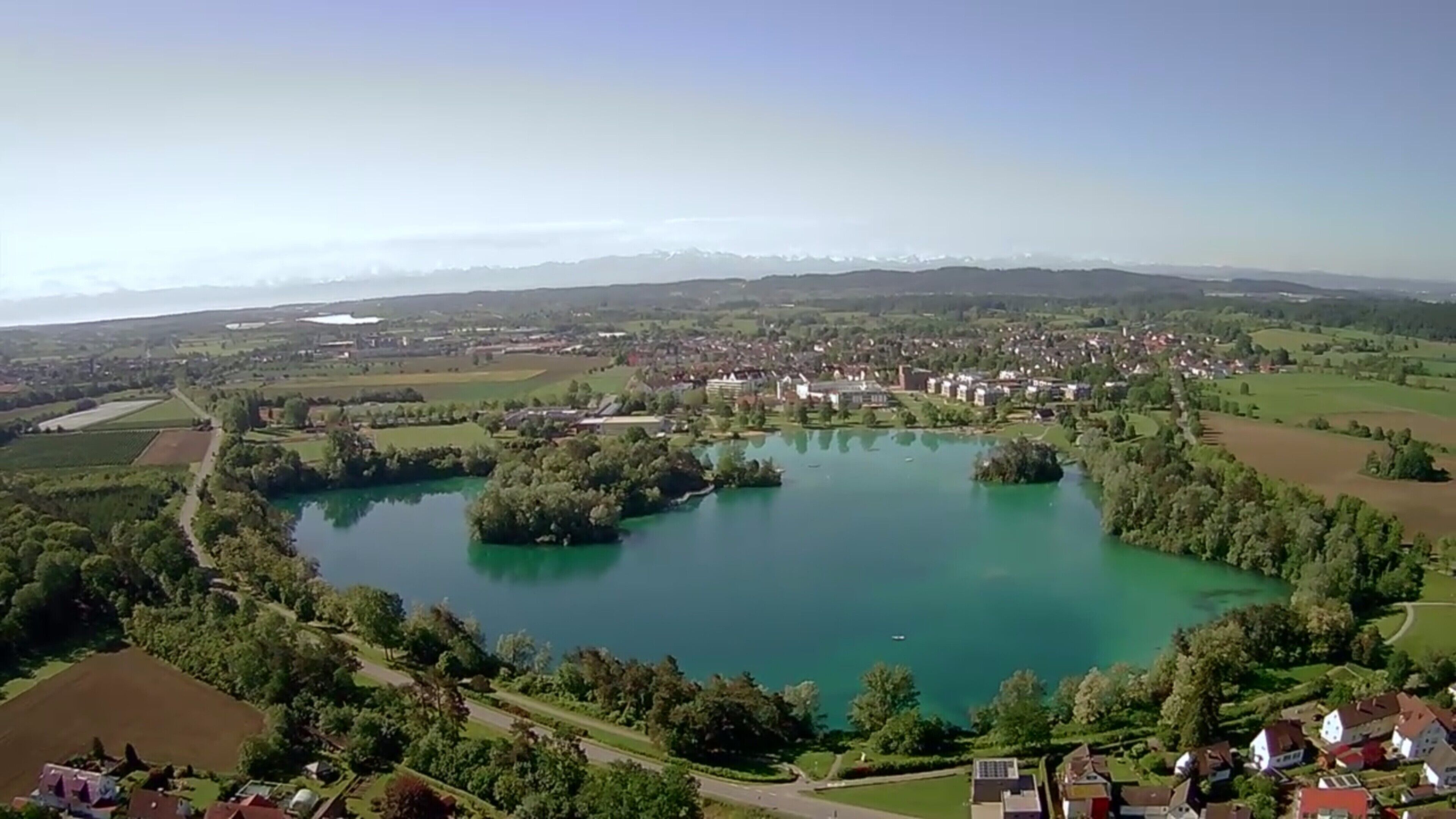 An aerial view of a town with a large lake, surrounded by greenery and residential areas.