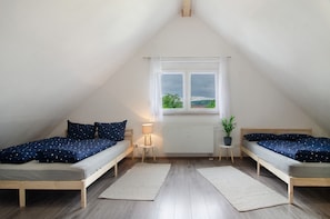 Et soveværelse med to senge i træ, et vindue med gardiner, en radiator, et lille bord med en lampe og en potteplante.