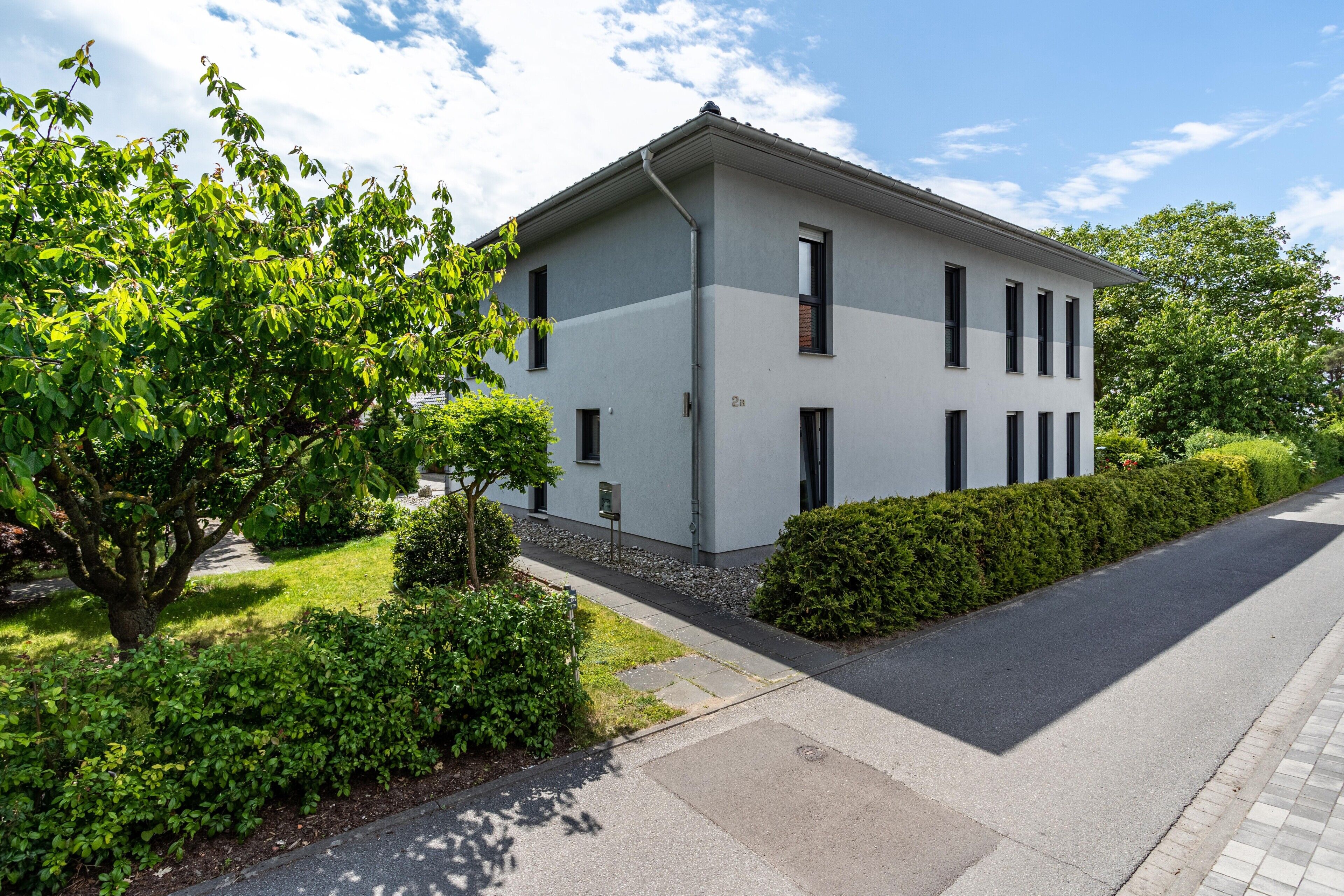 A modern two-story building with a flat roof, rectangular windows, and a paved driveway.