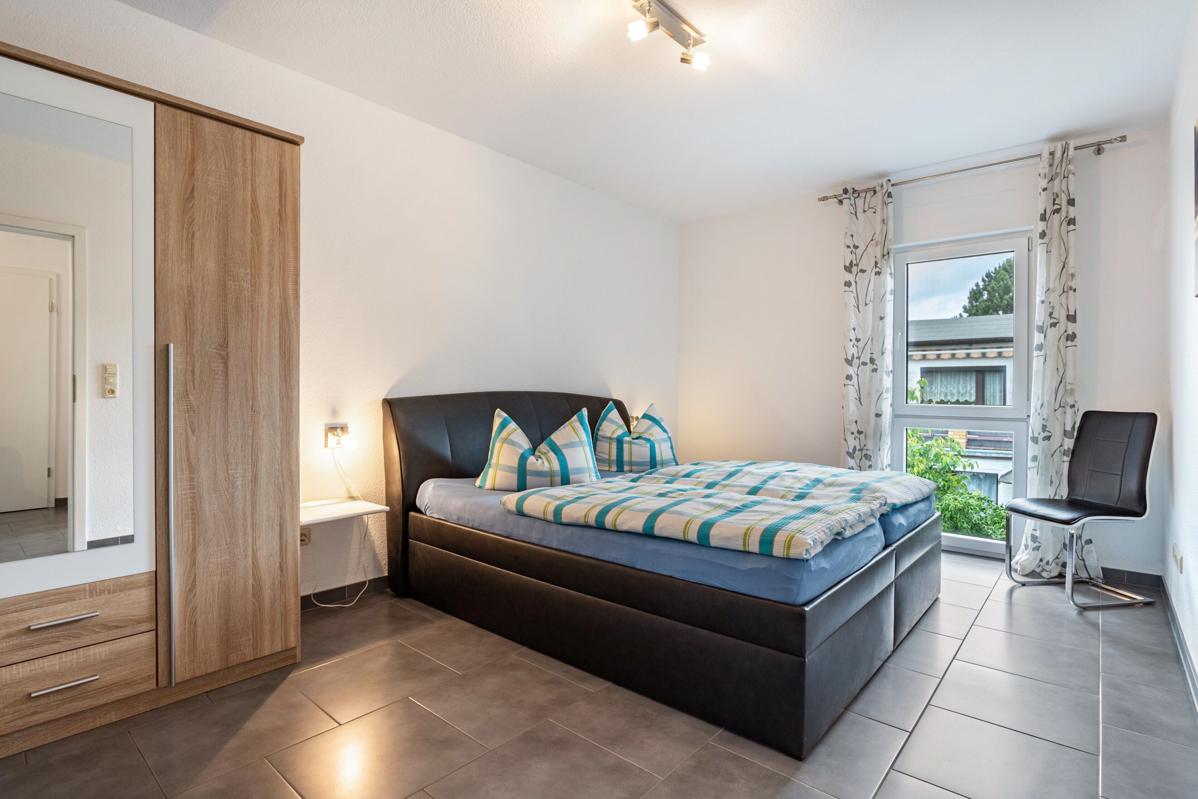 Une chambre à coucher avec un lit, une armoire, une chaise et une fenêtre avec des rideaux.