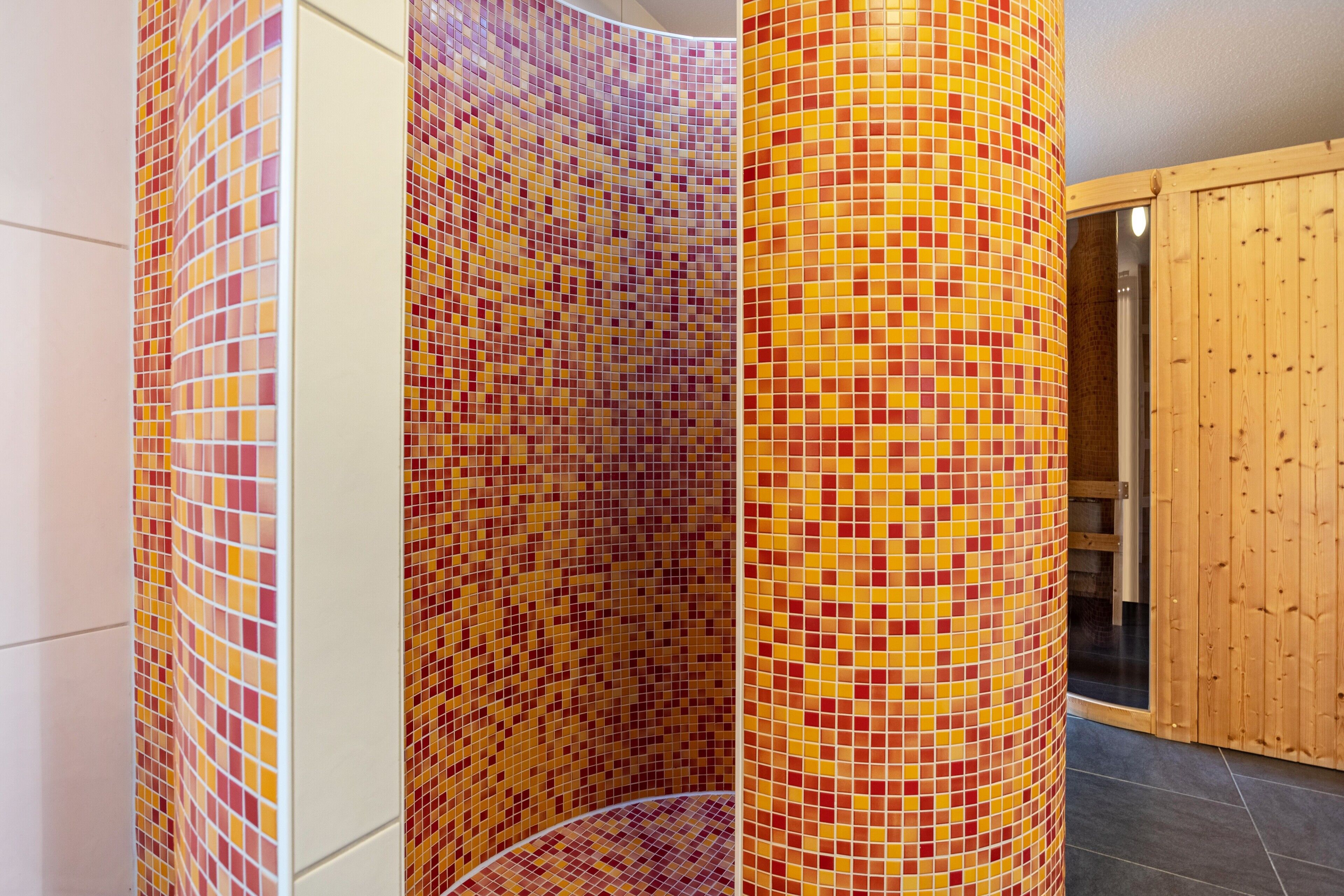 A bathroom with mosaic tile walls, a wooden door, and a tiled floor.