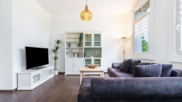 A modern living room with a flat-screen TV, a white cabinet, a sofa, and a hanging light fixture.