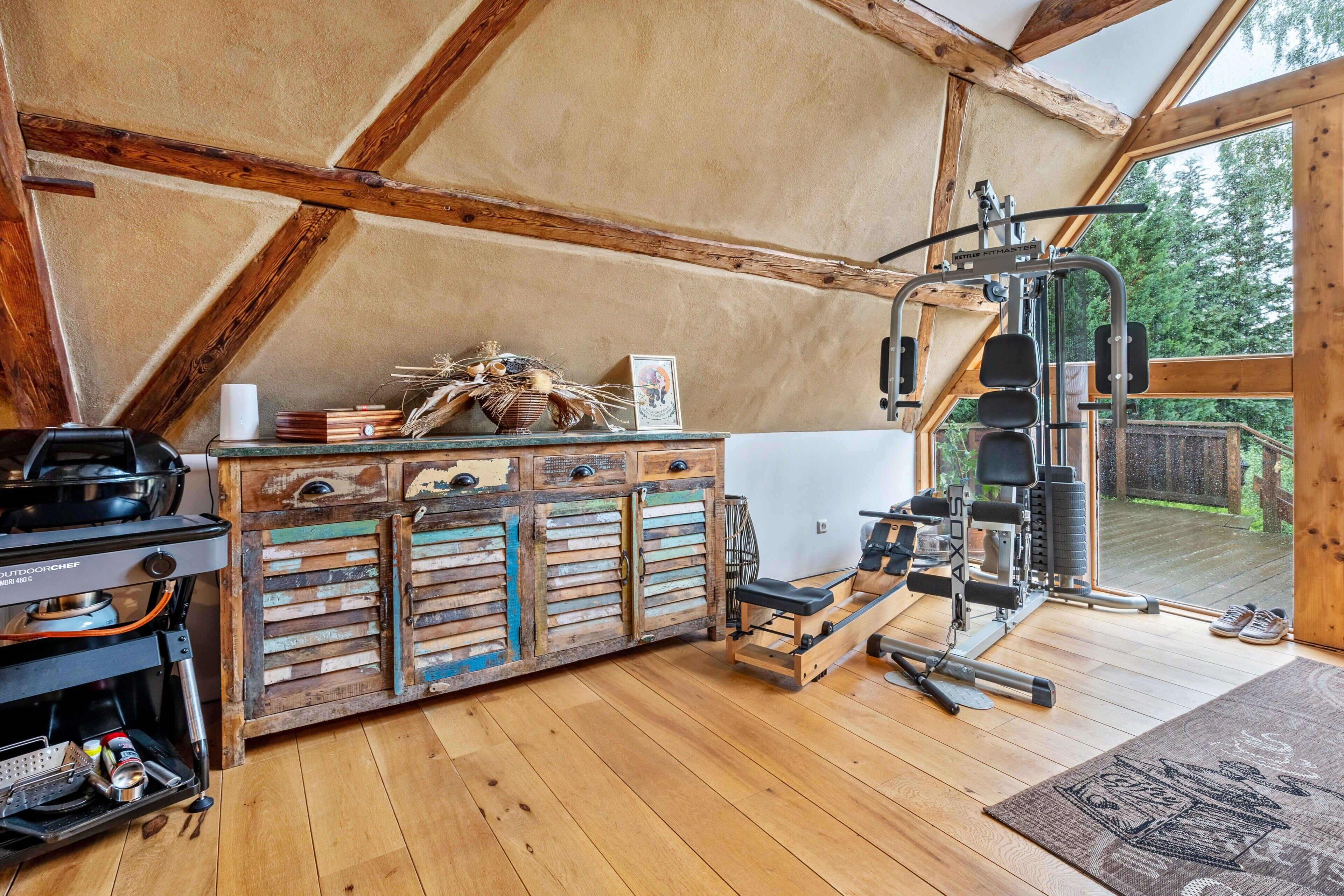 Una stanza rustica con travi in legno, angolo cottura, area fitness e vista sull'esterno.