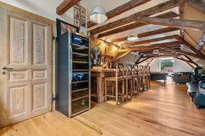 A rustic interior with exposed wooden beams, a wine refrigerator, and a dining area.