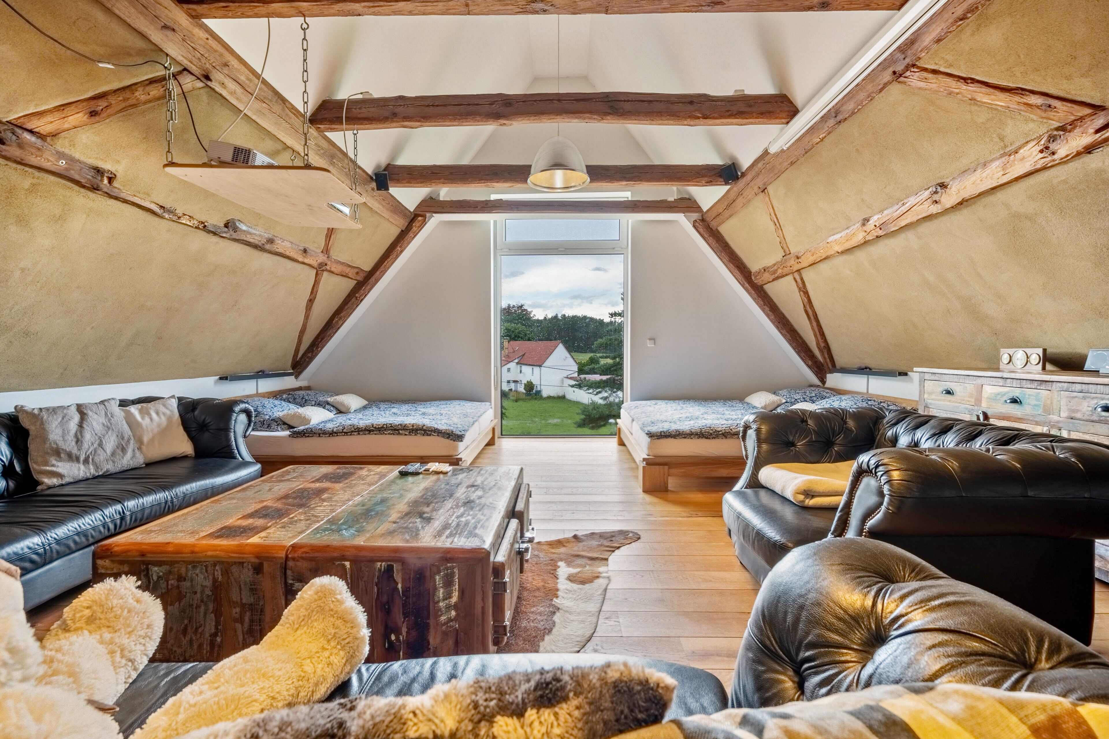 A loft-style room with a wooden ceiling, two leather sofas, a wooden coffee table, and a view of a house through a skylight.