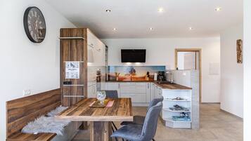 A modern kitchen with a wooden table, grey chairs, and a mounted flat-screen TV.