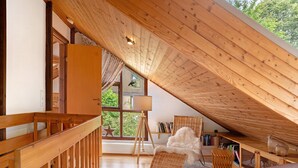 Ein gemütliches Dachzimmer mit Holzbalken, einem großen Fenster und Blick auf Grünflächen.