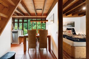 A bedroom with a wooden bed, a view of the outdoors, a dining area with chairs and a table, and a kitchen with a dishwasher. - Holiday Home 'Karlsminde' with Private Terrace, Garden, and Wi-Fi (Waabs)