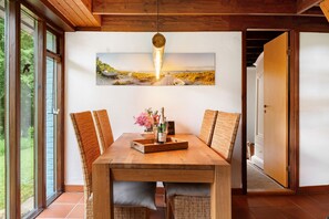 A dining area with a wooden table, wicker chairs, and a large landscape painting above. - Holiday Home 'Karlsminde' with Private Terrace, Garden, and Wi-Fi (Waabs)