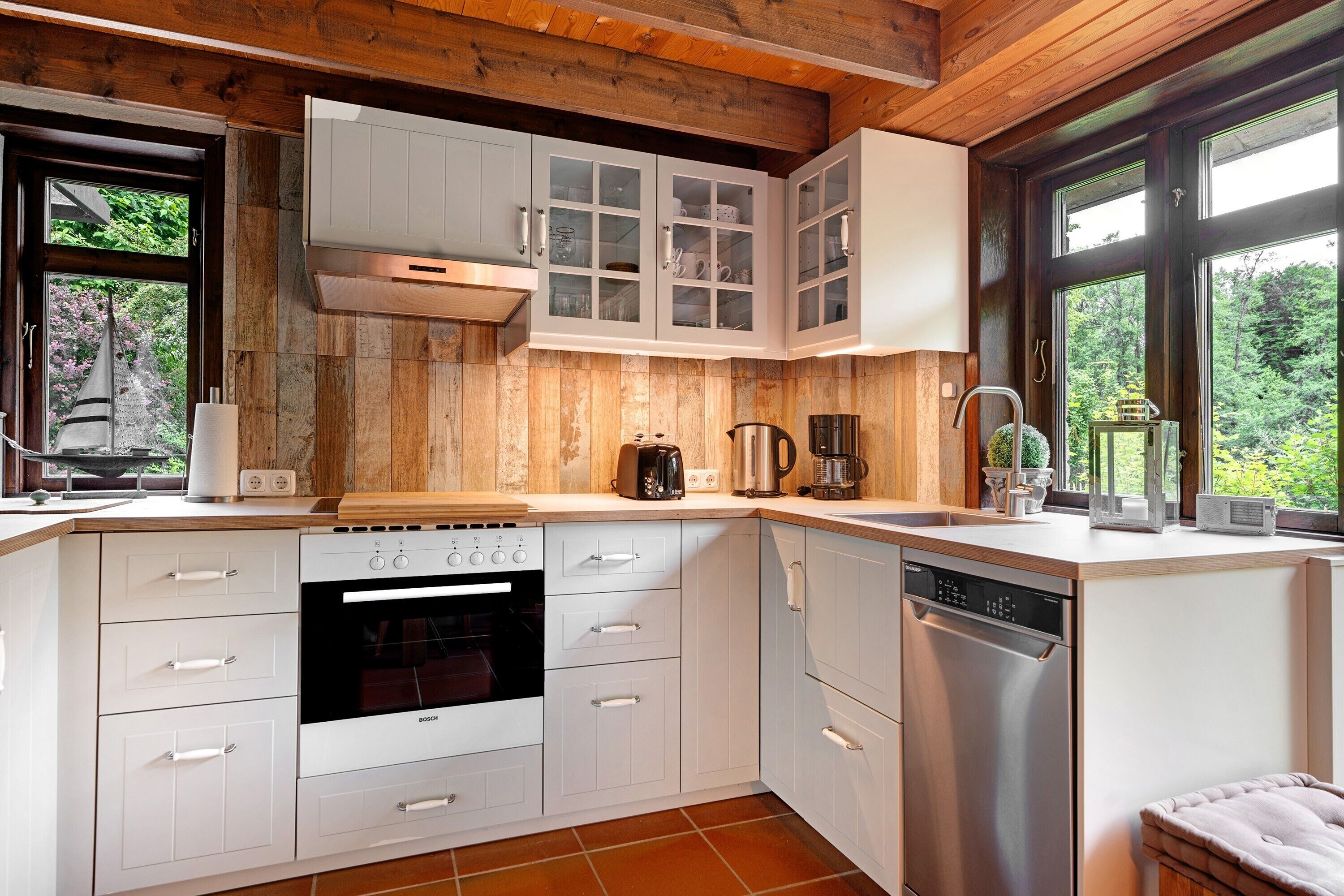 A modern kitchen with white cabinetry, a Bosch oven, a dishwasher, and a large window with a view of greenery.