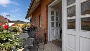 Une terrasse avec une table et des chaises, une porte et une vue sur un bâtiment en arrière-plan.