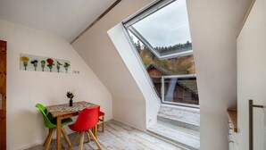 A room with a sloped ceiling, a dining table with chairs, a window with a view of a building and trees, and a wall-mounted light switch. - Apartment 'Burgblick' with Mountain View, Shared Garden and Wi-Fi (Hausach)
