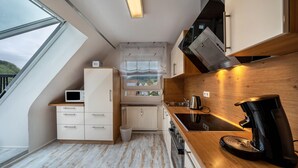A compact kitchen with a microwave, stove, and coffee maker, a window with a view, and a radiator. - Apartment 'Burgblick' with Mountain View, Shared Garden and Wi-Fi (Hausach)