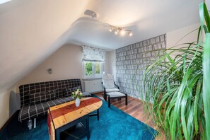 A cozy room with a black and white checkered sofa, a wooden table with a vase, a grey armchair, and a large green plant. - Apartment 'Burgblick' with Mountain View, Shared Garden and Wi-Fi (Hausach)