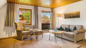 Une pièce chaleureuse avec un fauteuil à carreaux, un canapé, une petite table avec une lampe et une vue sur un balcon doté d’une balustrade.