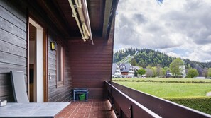 A wooden building with a balcony overlooking a green landscape and a hill.