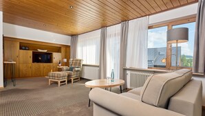 Een moderne woonkamer met een houten plafond, een bank, een ronde tafel, een televisie en een raam met gordijnen.