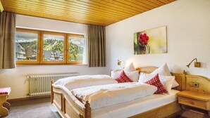 Een slaapkamer met twee bedden, een raam met uitzicht op huizen, een radiator en een schilderij aan de muur.