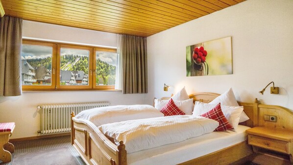 Une chambre avec deux lits, une fenêtre donnant sur des maisons, un radiateur et un tableau accroché au mur.