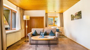 Un salon chaleureux avec un canapé, une table basse ronde, un lampadaire et une vue sur l’extérieur par une fenêtre.