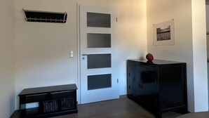 Una habitación con una puerta blanca, un armario negro y un estante fijado a la pared.