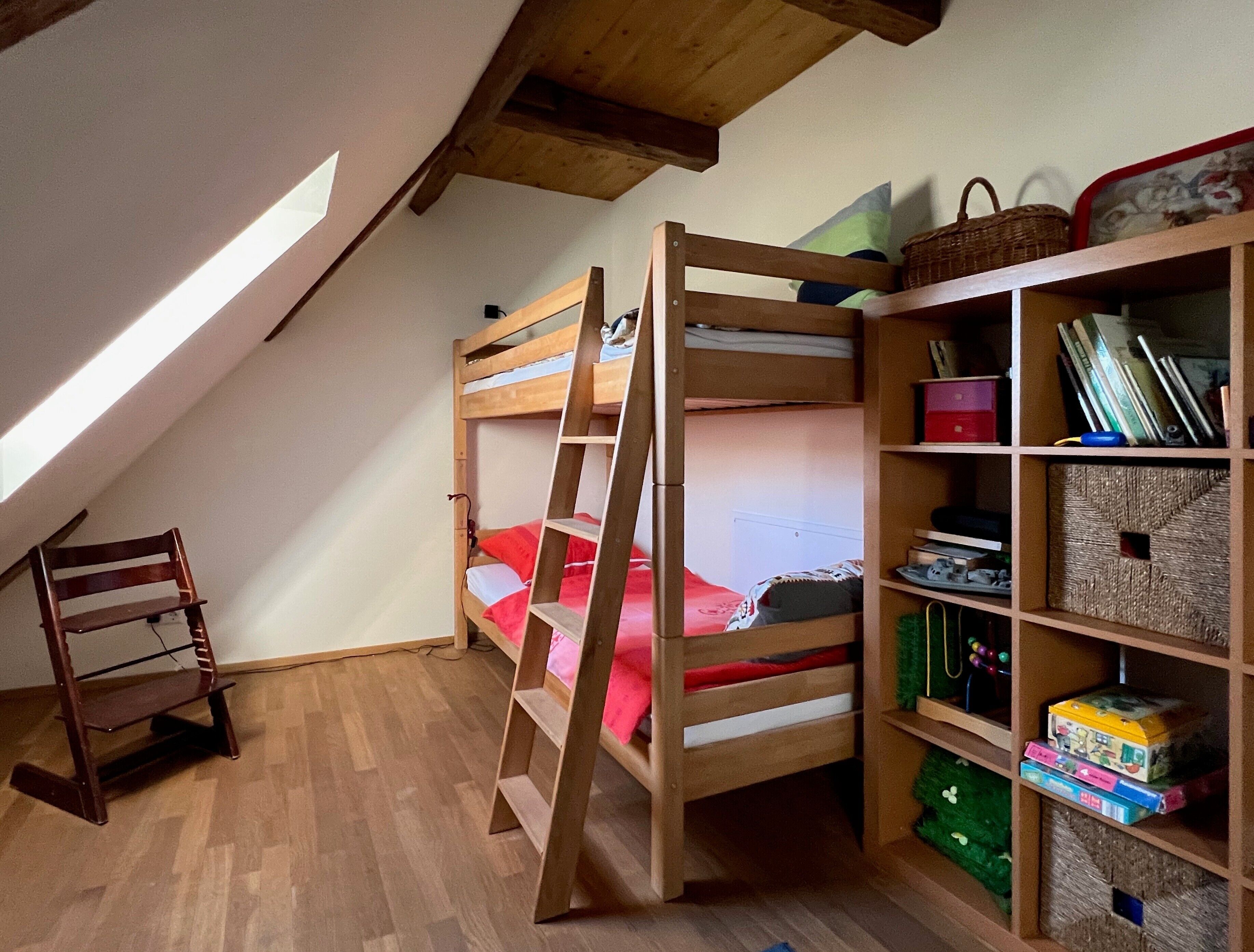 A bunk bed room with a ladder, a wooden chair, and a bookshelf with storage boxes.