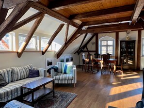 A loft-style room with exposed wooden beams, a sofa, a dining table with chairs, and a cabinet.