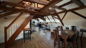 Un ático amplio con vigas de madera a la vista, una mesa de comedor con sillas, un sofá y una escalera.