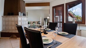A dining area with a wooden table set for four, a fireplace, and a view of the outside through a window. - Holiday Home 'Ferienhaus Am Rhein' with Private Terrace, Balcony and Wi-Fi (Rheinau)