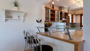 A modern kitchen with a glass-top island, stainless steel chairs, and a white shelf with decorative items. - Holiday Home 'Ferienhaus Am Rhein' with Private Terrace, Balcony and Wi-Fi (Rheinau)