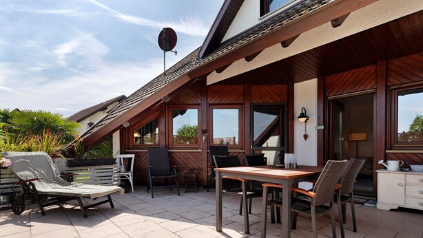 An outdoor patio area with a dining table, chairs, a lounge chair, and a satellite dish. - Holiday Home 'Ferienhaus Am Rhein' with Private Terrace, Balcony and Wi-Fi (Rheinau)