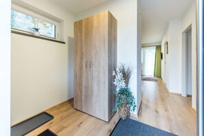 Ein Flur mit einem Holzschrank, einer Topfpflanze und einem Fenster mit Blick auf Bäume.