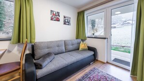A modern living room with a grey sofa, green curtains, a wooden chair, and a patterned rug.