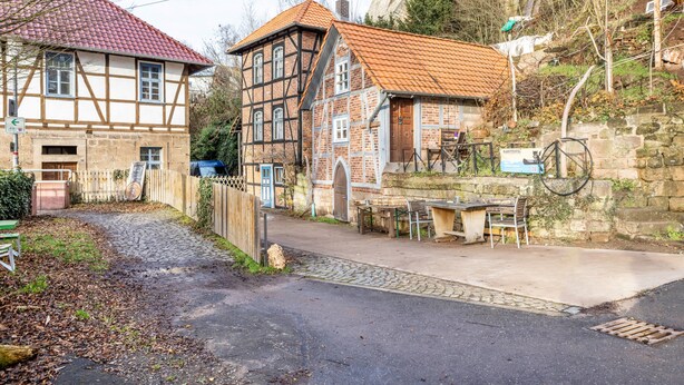 Una casa tradicional de entramado de madera con un sendero adoquinado, un muro de piedra y una bicicleta.