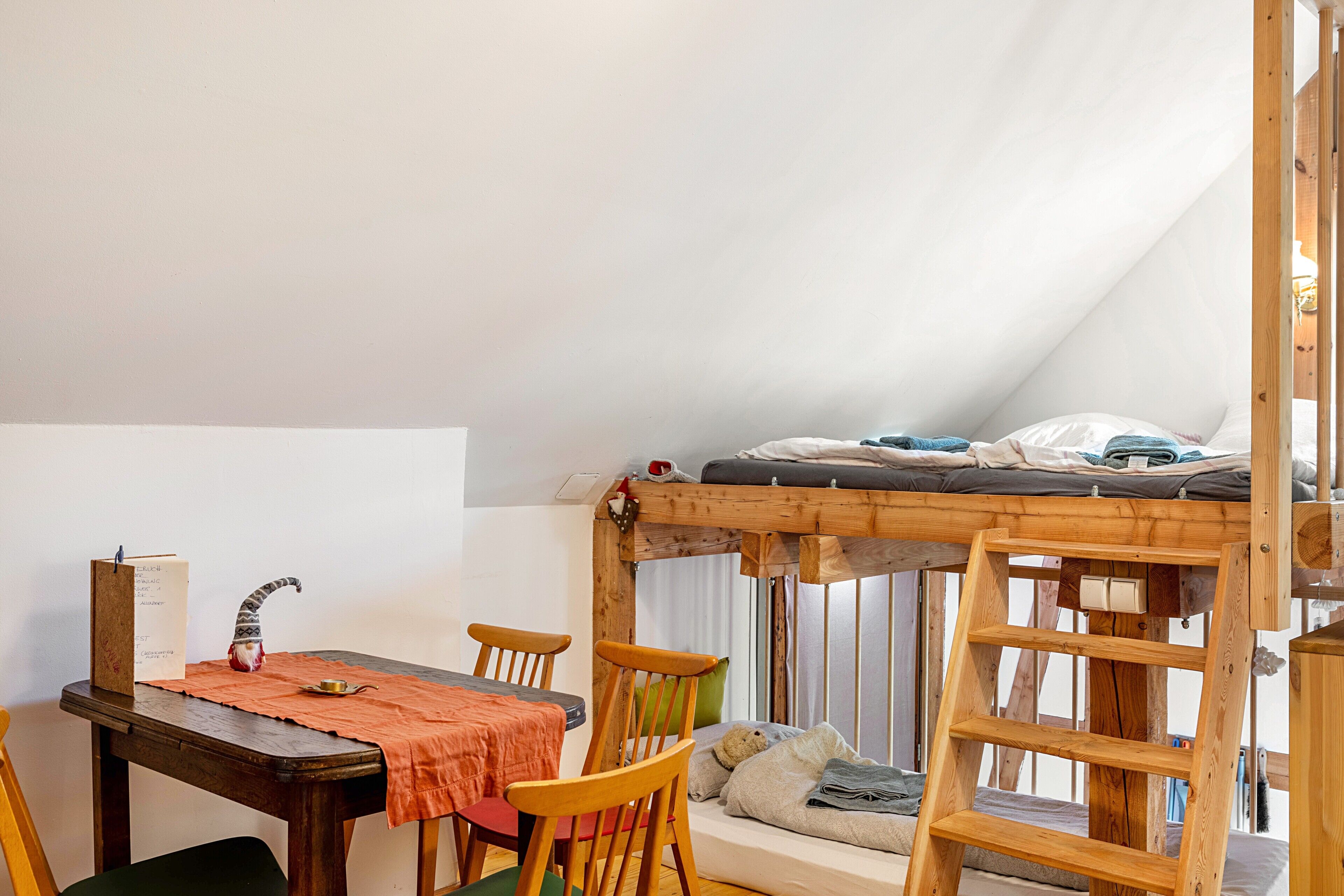 A room with a loft bed, a dining table with chairs, and a wooden ladder.