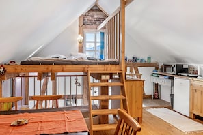 A loft bedroom with a wooden bunk bed, a kitchen area with a microwave and sink, and a window with curtains. - Holiday Home 'Tiny House An Der Werra' with Private Terrace, Wi-Fi and Air Conditioning (Bad Sooden-Allendorf)