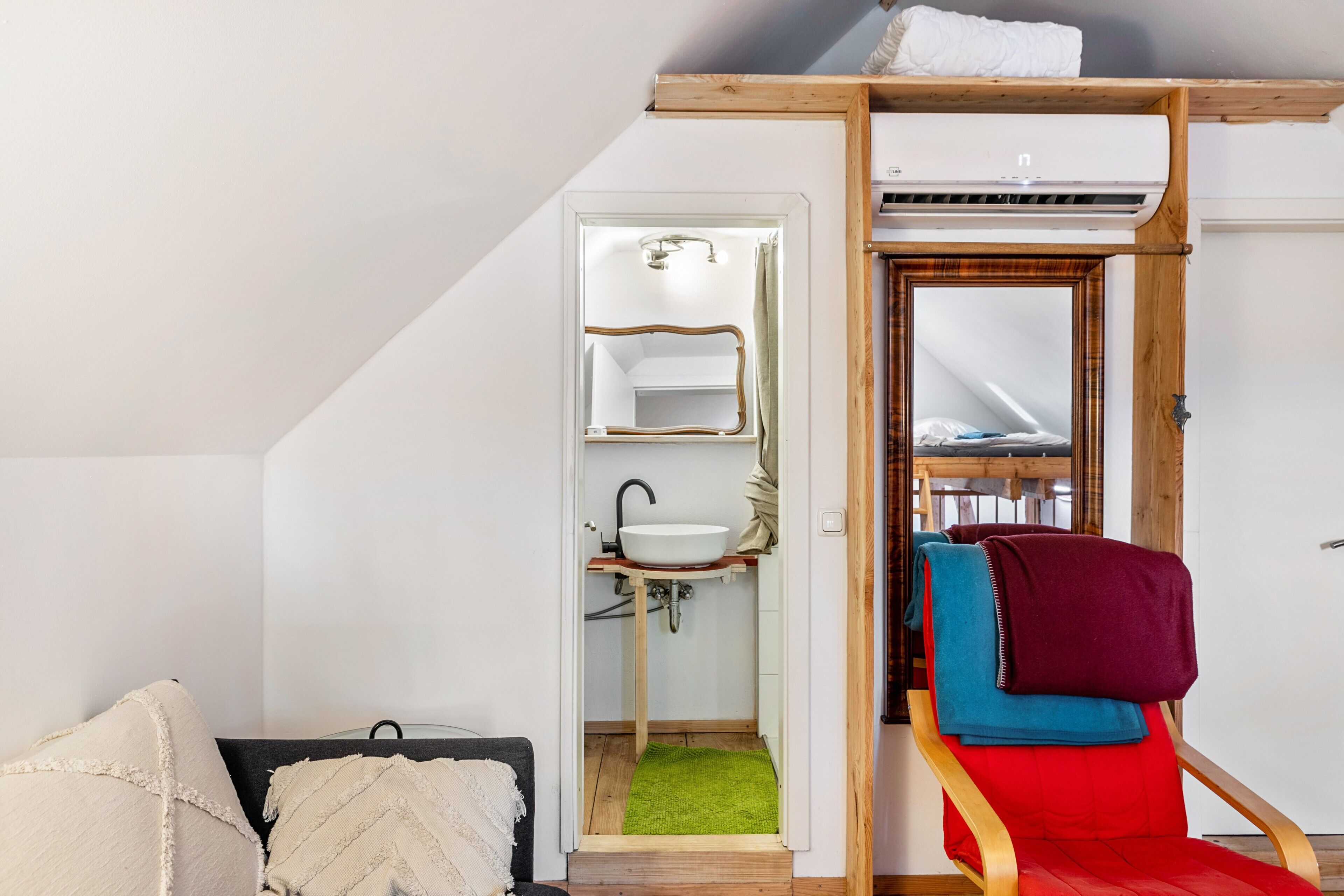 Habitación compacta con cama tipo litera, baño pequeño con lavamanos y una silla con mantas.