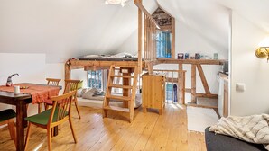 Habitación estilo loft con escalera de madera, literas, mesa de comedor con sillas y un sofá.