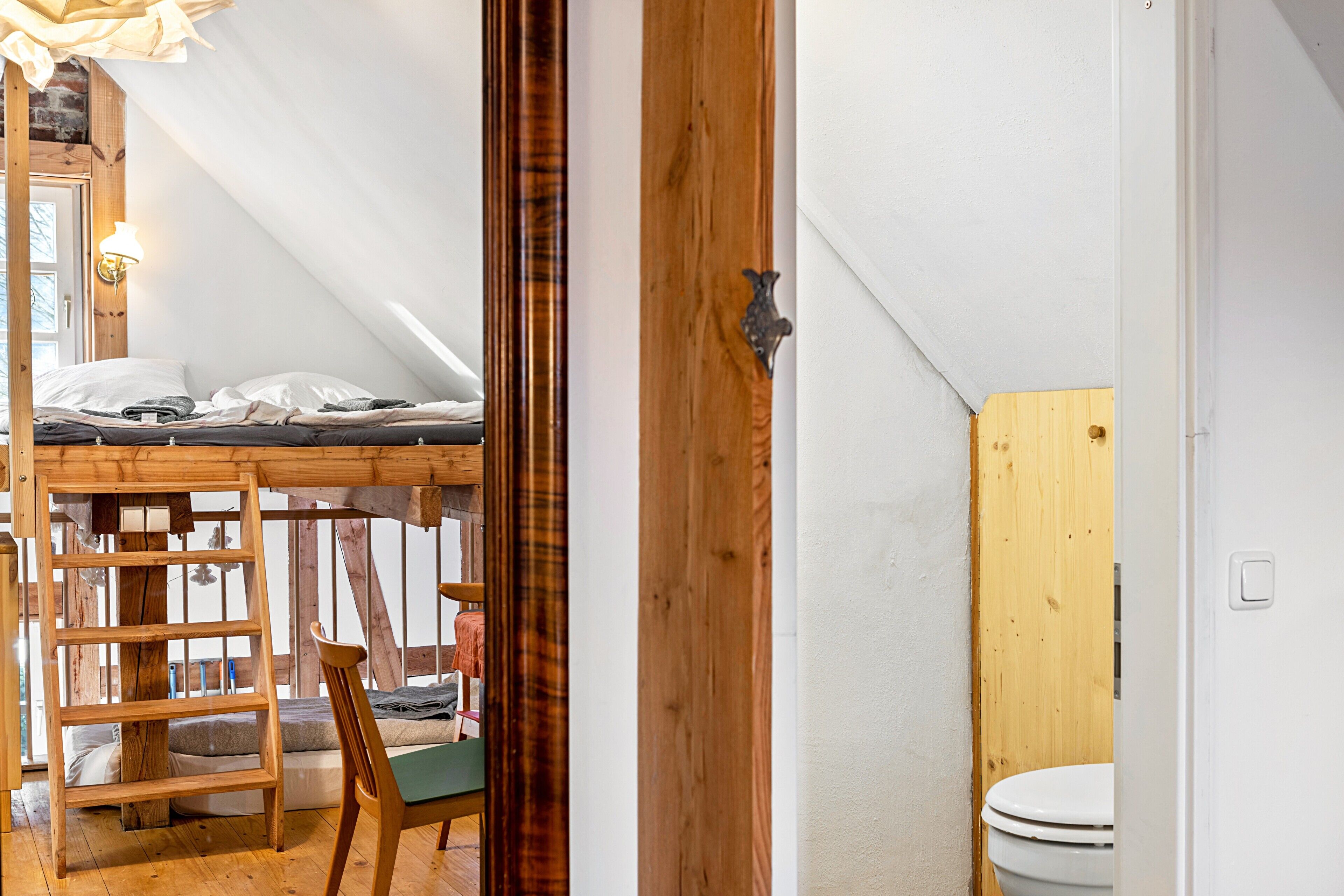 Une chambre à coucher aménagée en mezzanine, avec un escalier en bois, un lit superposé et une vue sur l’extérieur.