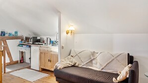 Un dormitorio estilo loft acogedor, con un sofá oscuro, una kitchenette pequeña y un techo blanco.