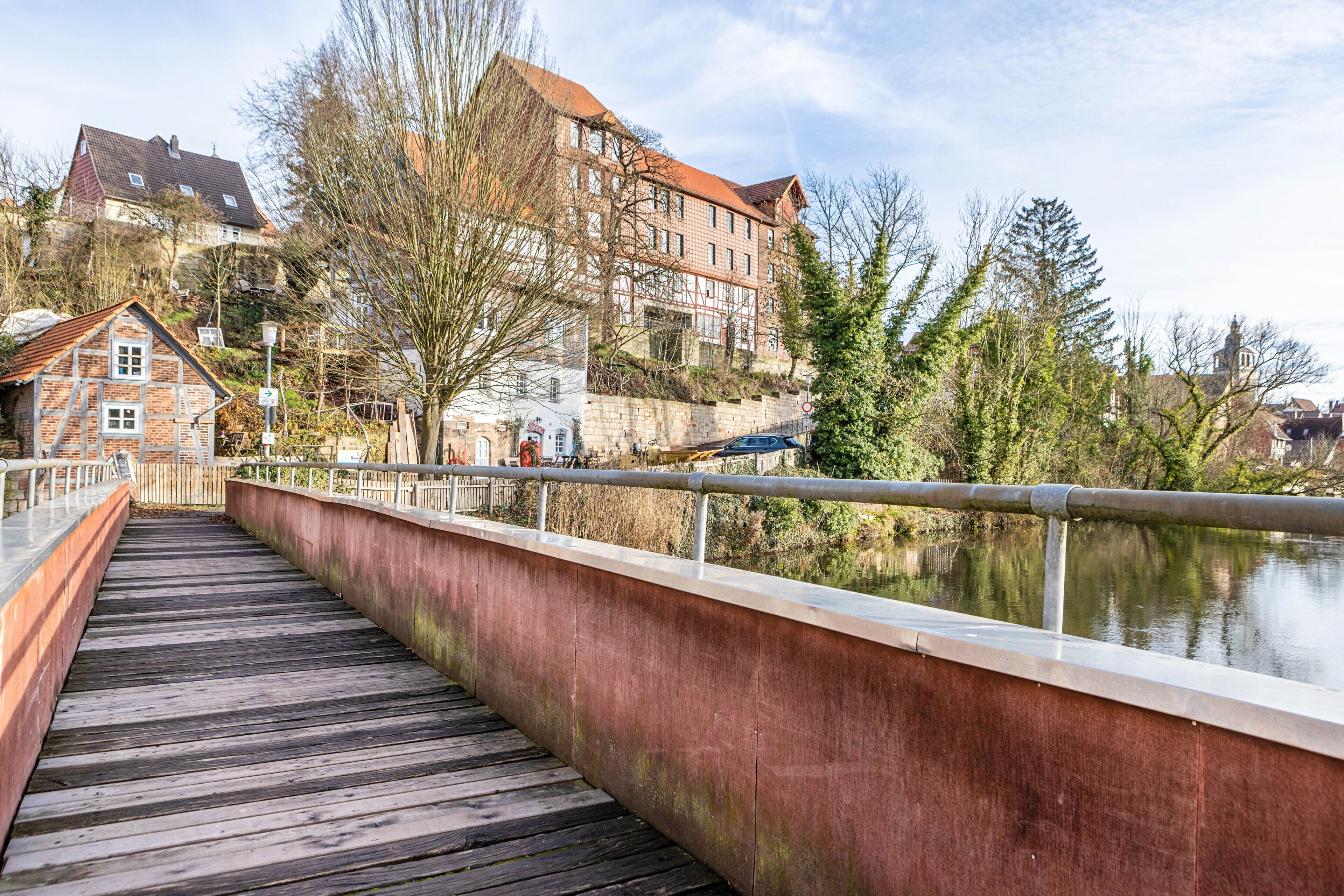 A wooden bridge with metal railings, a river, and buildings in the background.