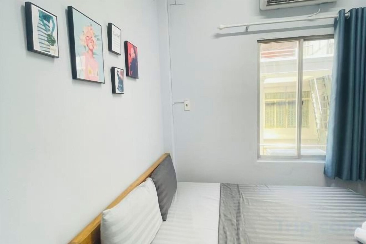 A room with a bed, a window with curtains, and wall-mounted artwork.