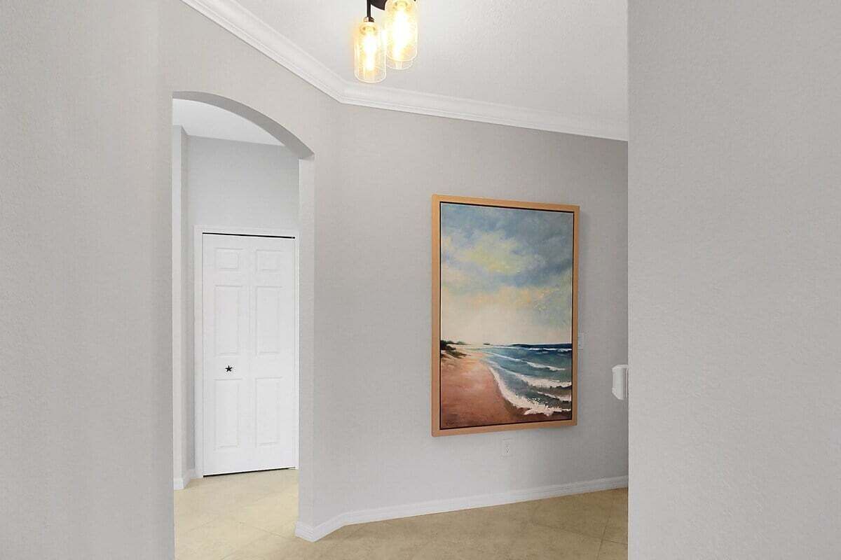 Un pasillo con una puerta blanca, un cuadro enmarco con una escena de playa y una lámpara con tres bombillas.