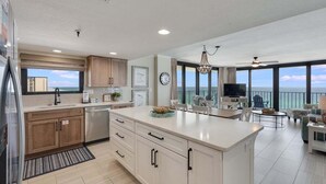 A modern kitchen with a large island, wooden cabinets, and a view of the ocean.