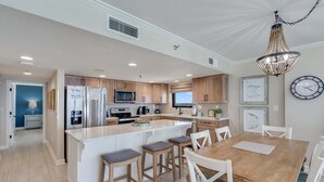 A modern kitchen with a central island, white cabinetry, and a dining area with a wooden table and white chairs.
