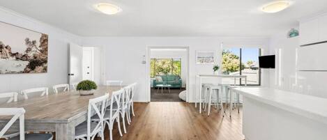 A modern kitchen with white cabinetry, a wooden dining table, and a view to the outside.