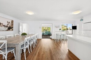 A modern kitchen with white cabinetry, a wooden dining table, and a view to the outside.