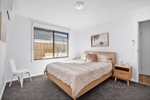 A bedroom with a large bed, a window, a chair, and a bedside table.
