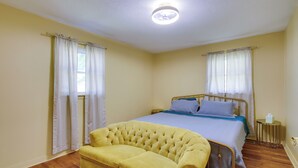 Una camera da letto con un letto, un divano giallo e un comodino.
